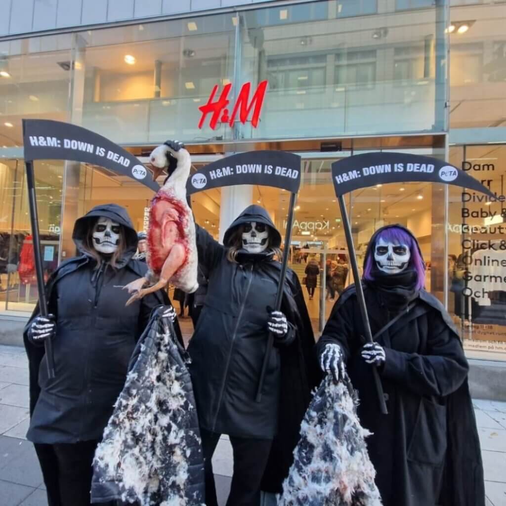 PETA supporters in skull face paint hold scythes reading "H&M: Down is Dead"