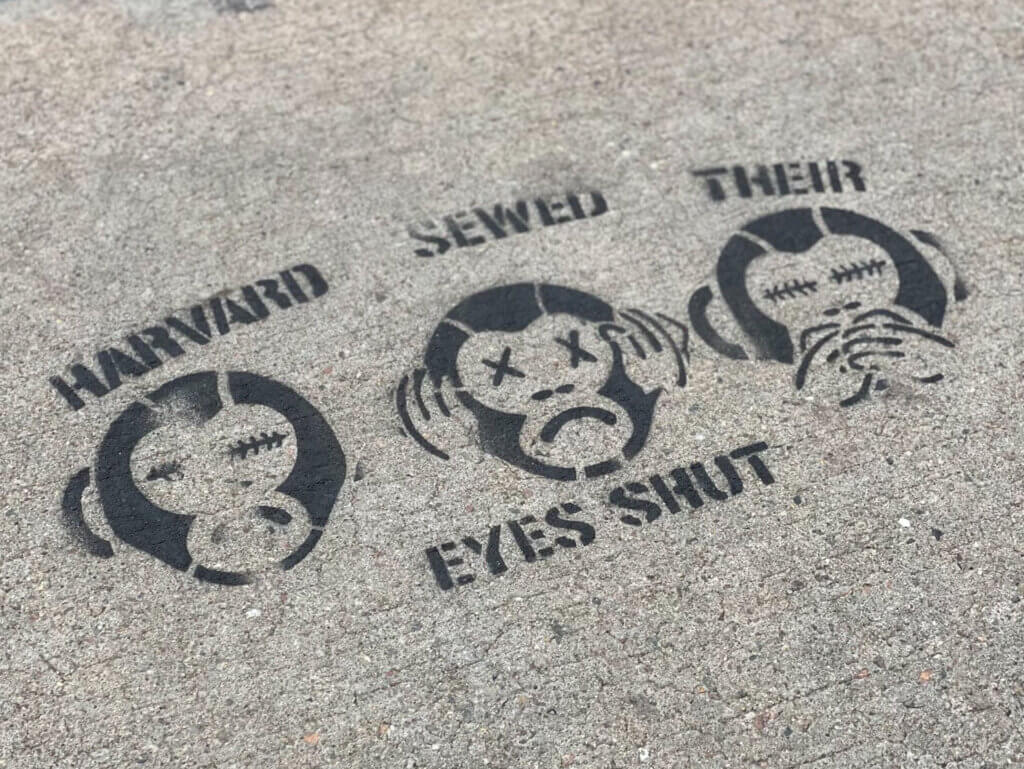 Stencil on concrete showing illustrations of three monkeys with text reading "Harvard sewed their eyes shut"