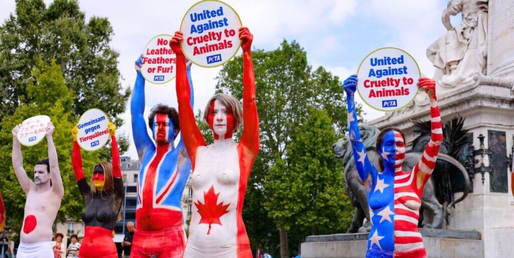 protesters bodypainted in different national flags hold up signs saying "no leather, feathers, or fur"