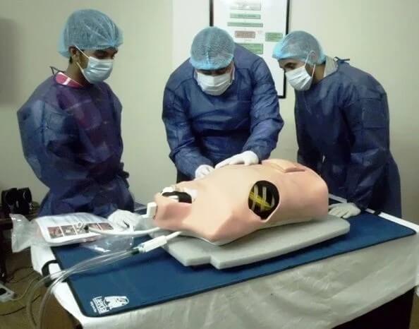 Three people in surgical scrubs leaning over a traumaman