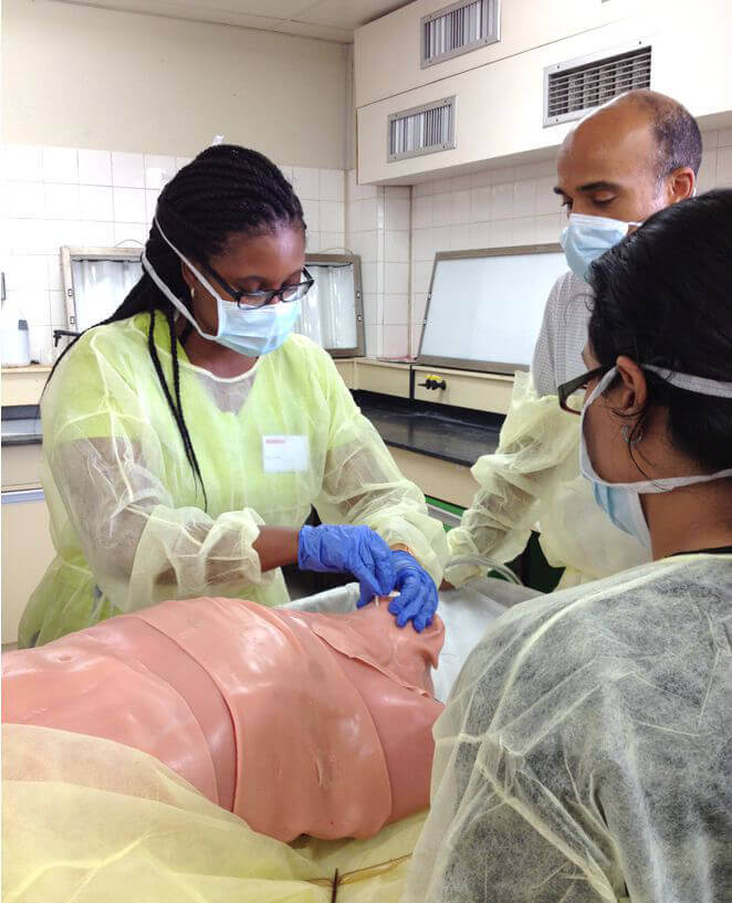 People in masks and scrubs standing over a traumaman simulator