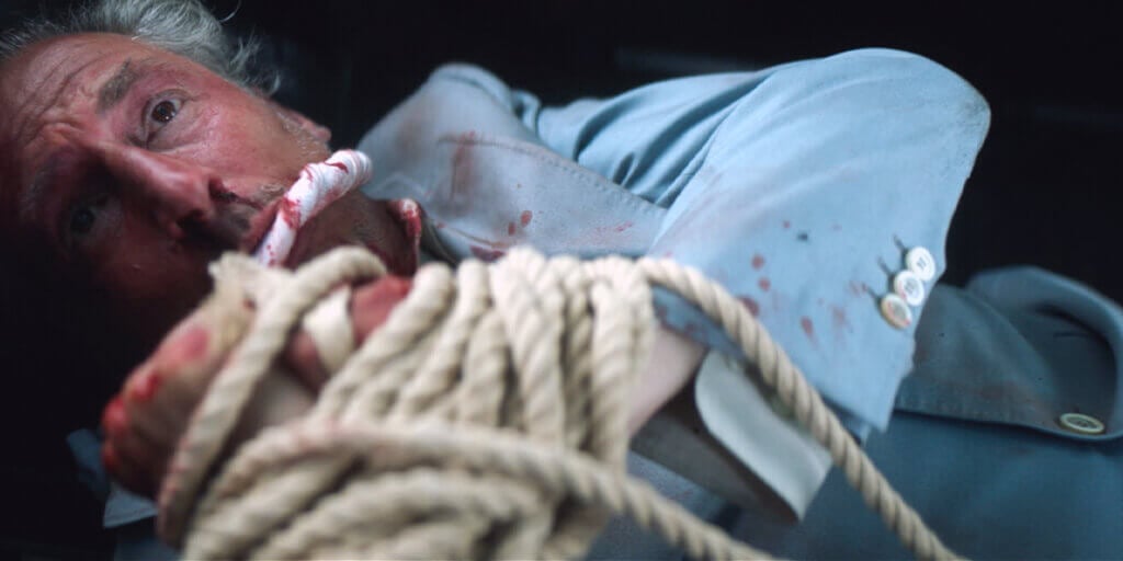 A man with a scared expression tied up in the backseat of a car, portraying a scene from Mindful Mobsters.